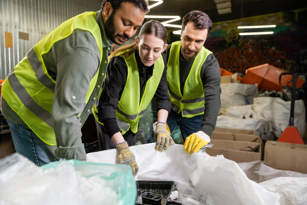 Young female worker in high visibility jacket and gloves looking at sacks while working together